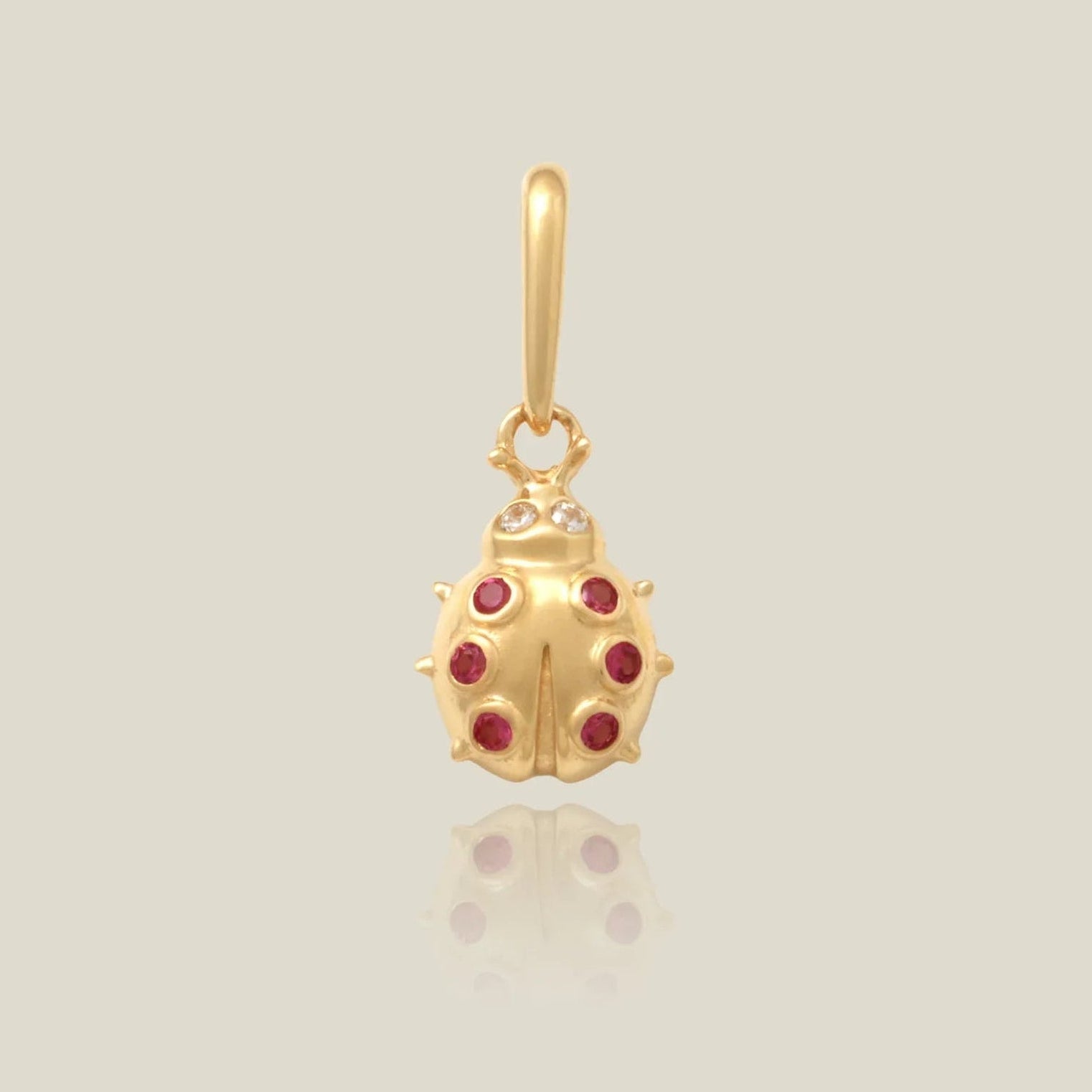 Gold ladybug pendant with red gemstones on a light beige background