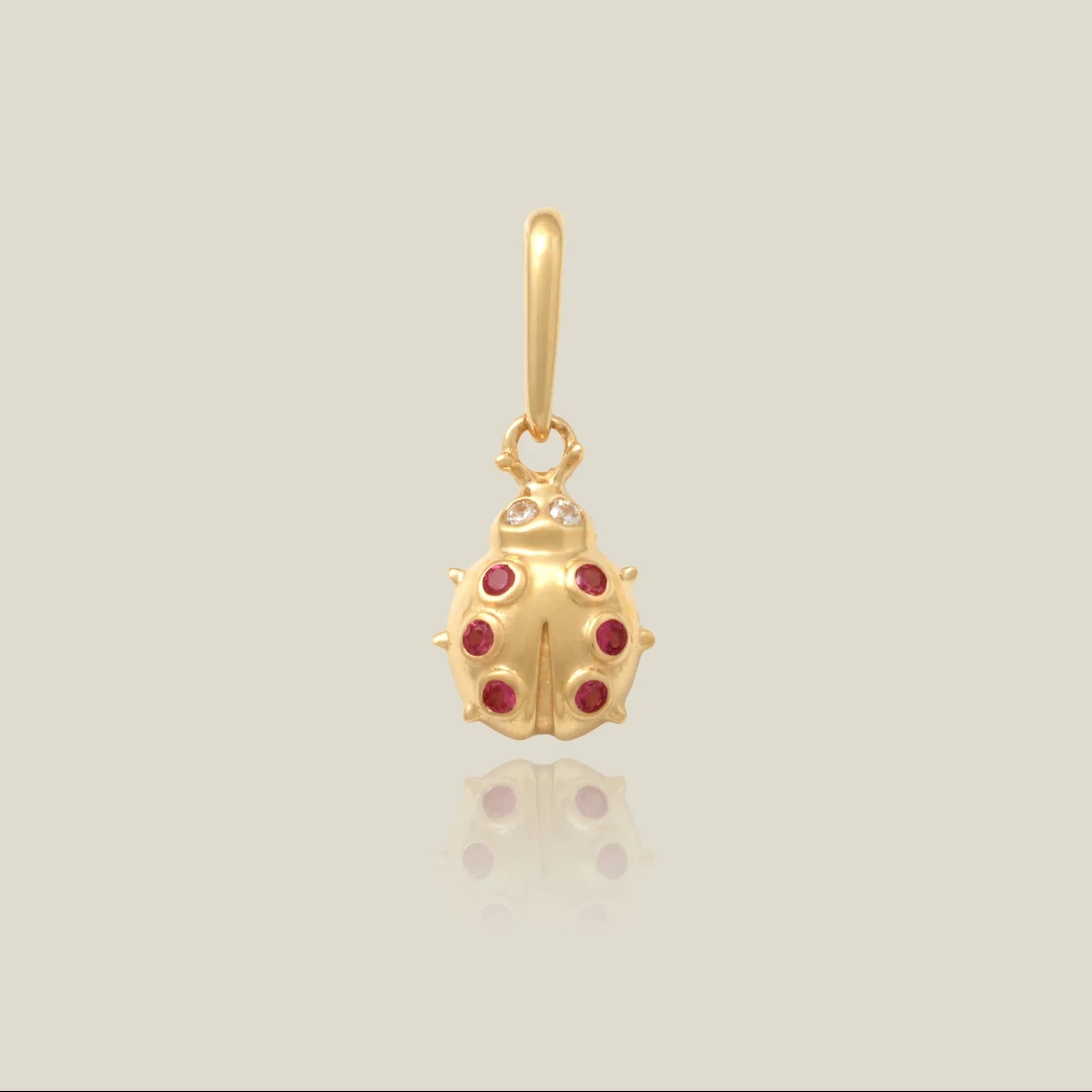 Gold ladybug pendant with red gemstones on a light beige background